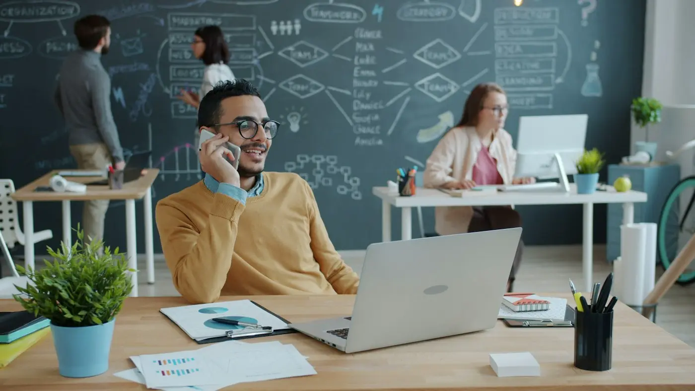 A person on the phone in an office, with colleagues at desks